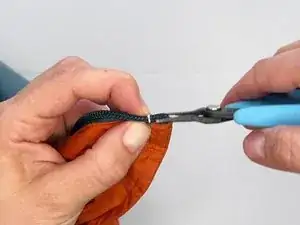 Use pliers to bend the prongs of the stop inward, clamping them around the zipper coil. The prongs will grab into the coil, securing it in place.